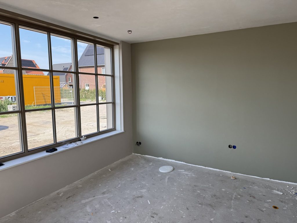 Nieuwbouwkamer met een groot raam en een egaal afgewerkte wand in een grijsgroene kleur