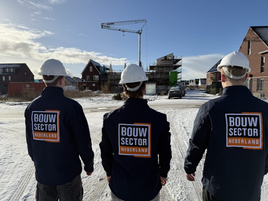 Drie vakmensen van Bouwsector Nederland met witte helm voor een bouwkraan en nieuwbouwwoningen in aanbouw