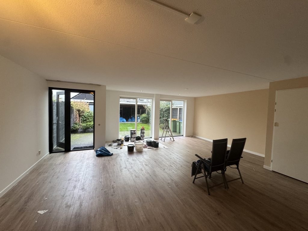 Lege woonkamer van een eengezinswoning met tuindeuren, houten vloer en verfspullen klaar voor het werk